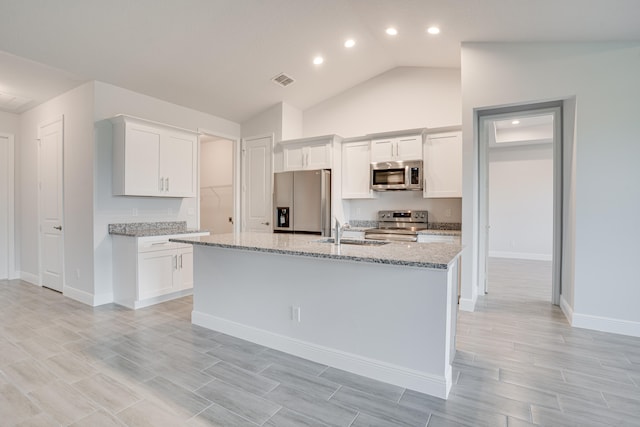 kitchen with a center island with sink, appliances with stainless steel finishes, light stone countertops, white cabinets, and lofted ceiling