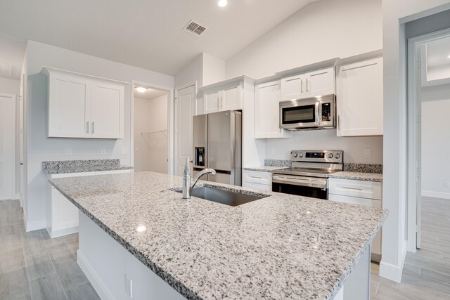 kitchen with white cabinets, stainless steel appliances, a kitchen island with sink, and vaulted ceiling