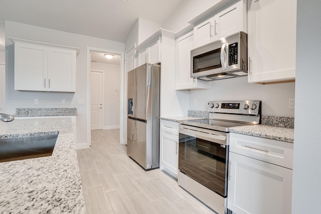 kitchen with appliances with stainless steel finishes, light stone countertops, sink, white cabinets, and light hardwood / wood-style flooring