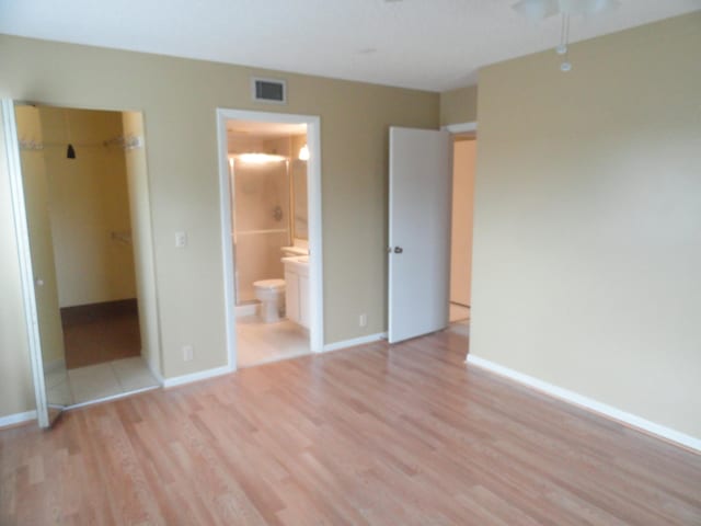 unfurnished bedroom featuring light hardwood / wood-style floors, a spacious closet, a closet, and ensuite bath