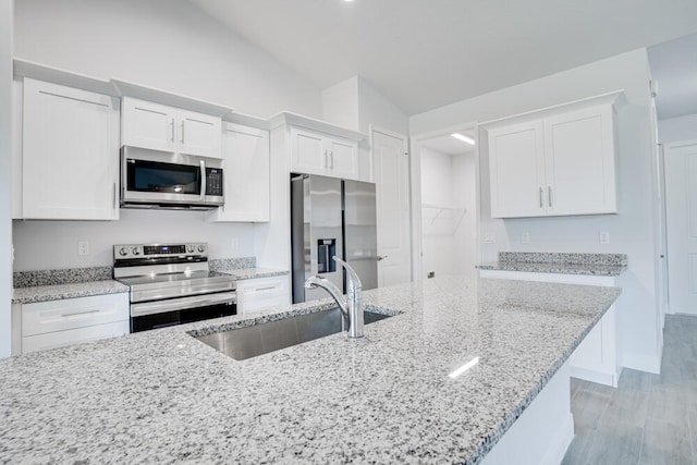 kitchen featuring white cabinetry, appliances with stainless steel finishes, lofted ceiling, and light wood-type flooring