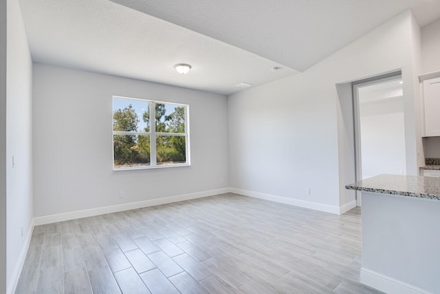 unfurnished room with light hardwood / wood-style floors, a textured ceiling, and vaulted ceiling