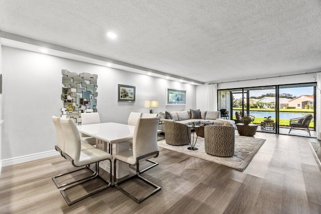 dining space with a textured ceiling, a water view, and light hardwood / wood-style flooring