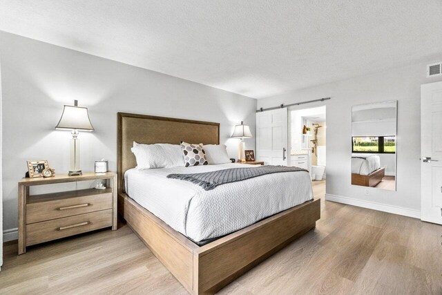 bedroom featuring a barn door, light hardwood / wood-style flooring, and a textured ceiling