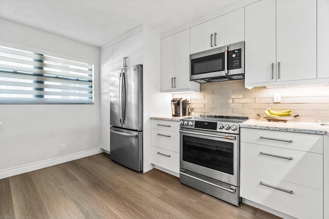 kitchen featuring hardwood / wood-style floors, backsplash, white cabinets, appliances with stainless steel finishes, and light stone counters