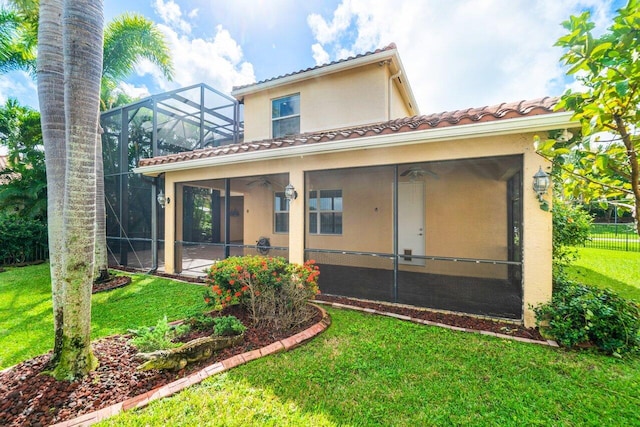 rear view of property with ceiling fan, a yard, and glass enclosure