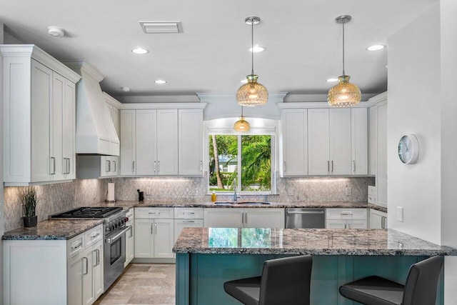 kitchen featuring pendant lighting, premium range hood, appliances with stainless steel finishes, white cabinetry, and a breakfast bar area