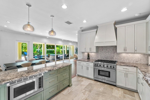 kitchen with decorative backsplash, appliances with stainless steel finishes, custom exhaust hood, pendant lighting, and white cabinets