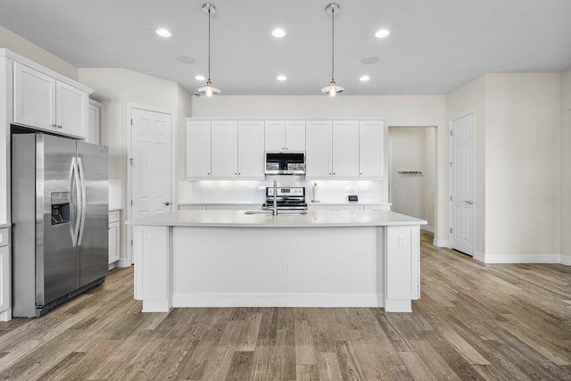 kitchen featuring white cabinetry, a kitchen island with sink, decorative light fixtures, and appliances with stainless steel finishes