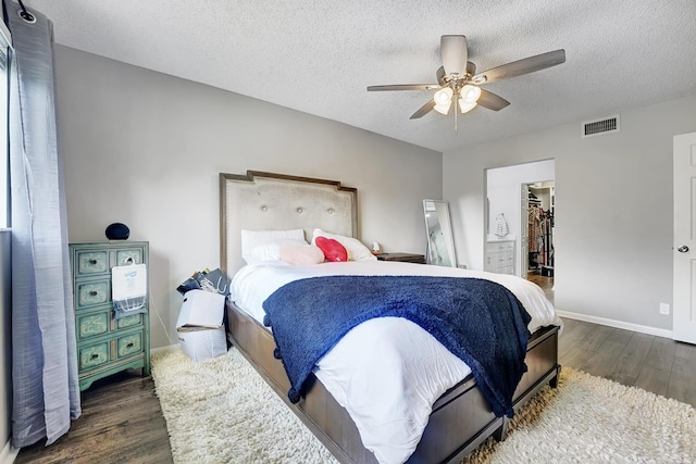 bedroom with ceiling fan, a spacious closet, a textured ceiling, dark hardwood / wood-style flooring, and a closet