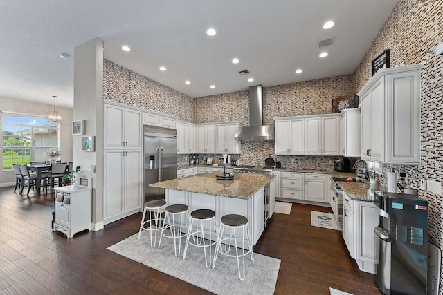 kitchen with stainless steel appliances, wall chimney exhaust hood, a kitchen island, and dark hardwood / wood-style flooring