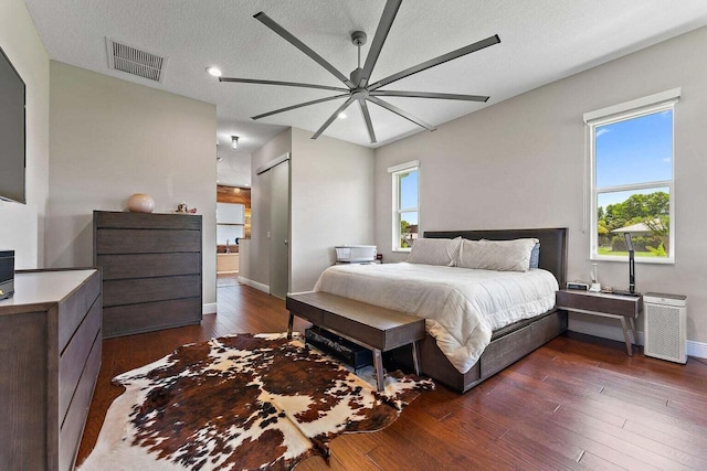 bedroom featuring dark wood-type flooring, multiple windows, a textured ceiling, and ceiling fan