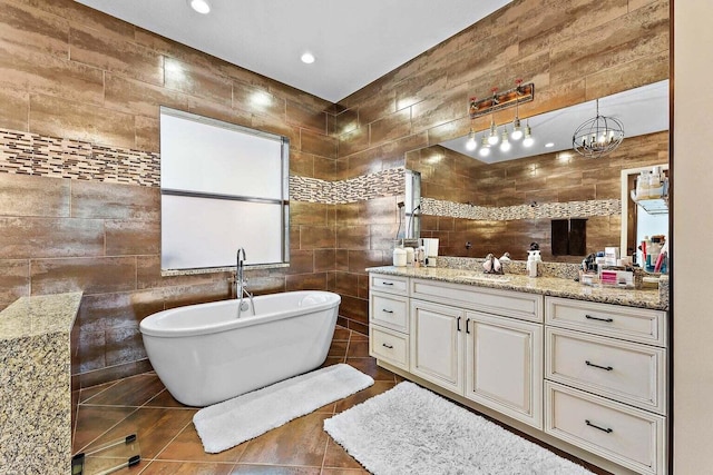 bathroom with tile patterned flooring, a chandelier, vanity, a bathing tub, and tile walls