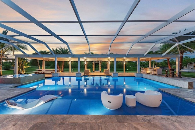 pool at dusk with exterior bar, a patio area, and a lanai