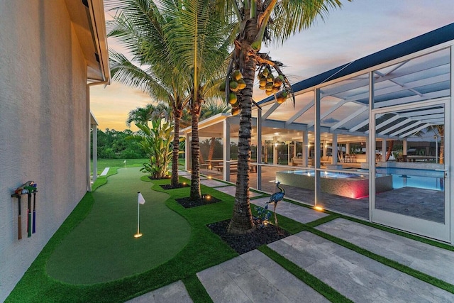 yard at dusk with a patio, glass enclosure, and a pool with hot tub