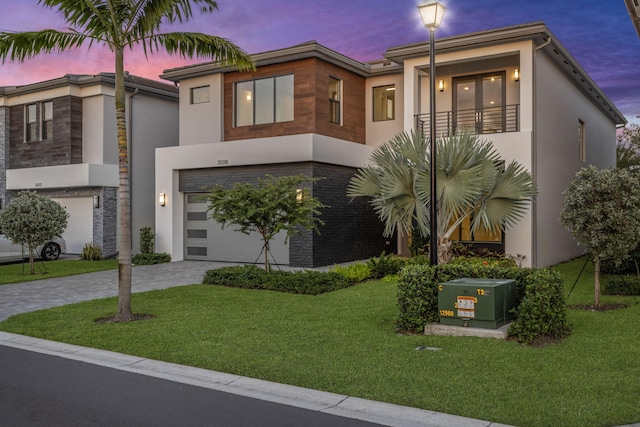 view of front of property featuring a garage, a balcony, and a yard