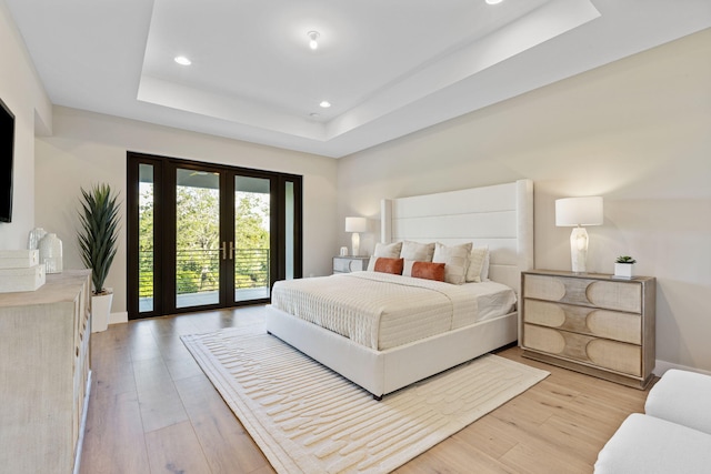 bedroom with a tray ceiling, french doors, light hardwood / wood-style floors, and access to exterior