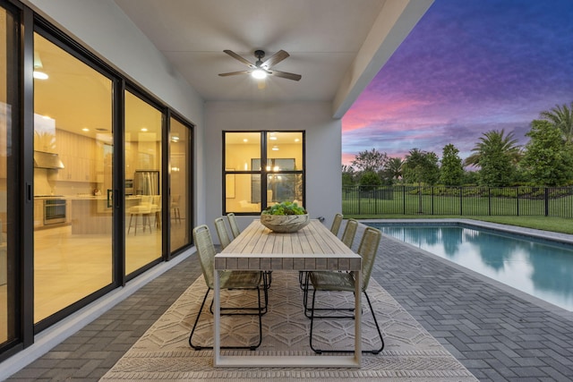 pool at dusk featuring ceiling fan and a patio area