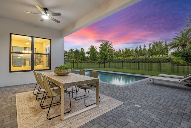 pool at dusk featuring ceiling fan, a yard, and a patio