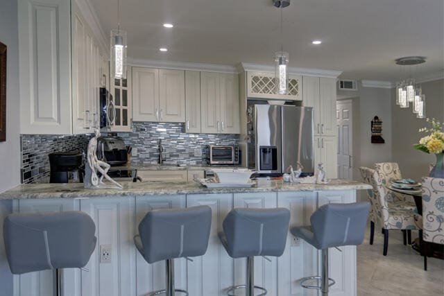 kitchen featuring light stone countertops, appliances with stainless steel finishes, hanging light fixtures, and ornamental molding