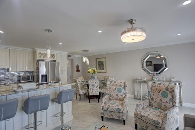 kitchen featuring stainless steel refrigerator with ice dispenser, decorative light fixtures, cream cabinetry, backsplash, and light stone counters