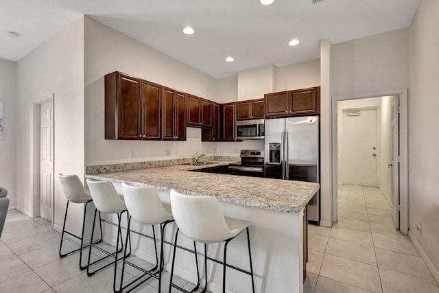 kitchen featuring sink, kitchen peninsula, a breakfast bar area, light tile patterned floors, and appliances with stainless steel finishes