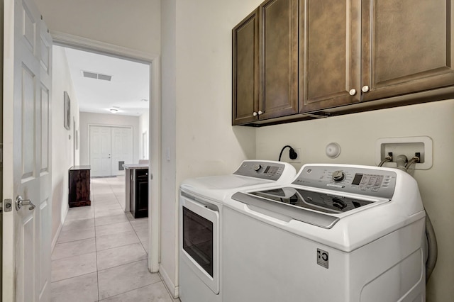 washroom featuring washing machine and dryer, light tile patterned flooring, and cabinets