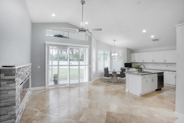 kitchen with a stone fireplace, white cabinetry, a healthy amount of sunlight, and an island with sink