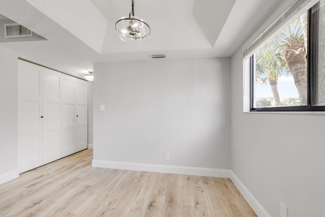 unfurnished bedroom featuring a raised ceiling, a closet, light hardwood / wood-style floors, and an inviting chandelier