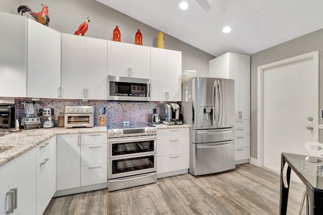 kitchen featuring white cabinetry, stainless steel appliances, light stone counters, light hardwood / wood-style floors, and decorative backsplash