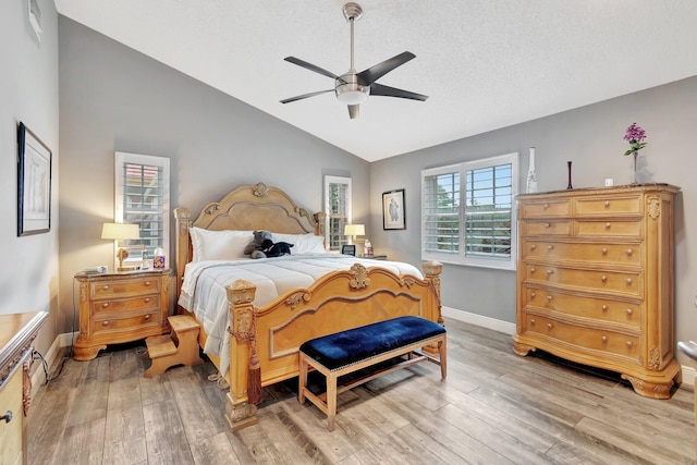 bedroom with ceiling fan, light wood-type flooring, lofted ceiling, and a textured ceiling