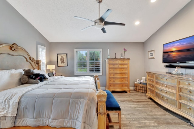 bedroom with a textured ceiling, ceiling fan, light hardwood / wood-style flooring, and lofted ceiling