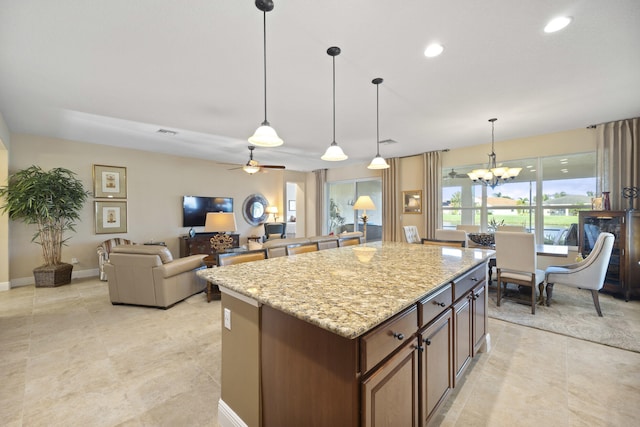 kitchen featuring light stone countertops, ceiling fan with notable chandelier, pendant lighting, and a kitchen island