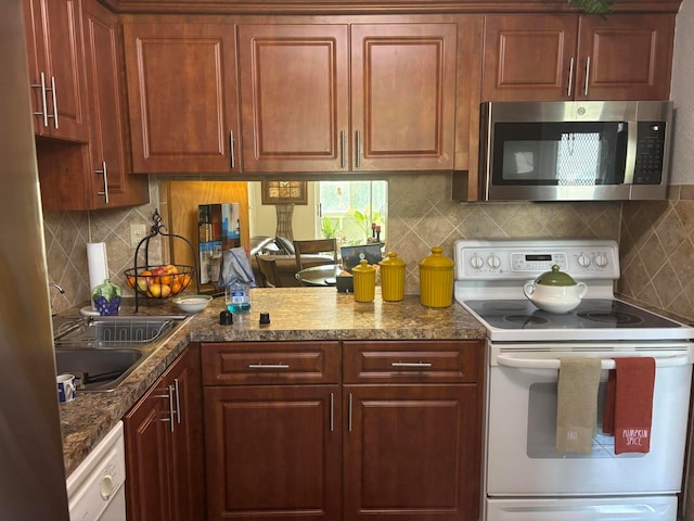 kitchen featuring white appliances, dark stone countertops, sink, and backsplash