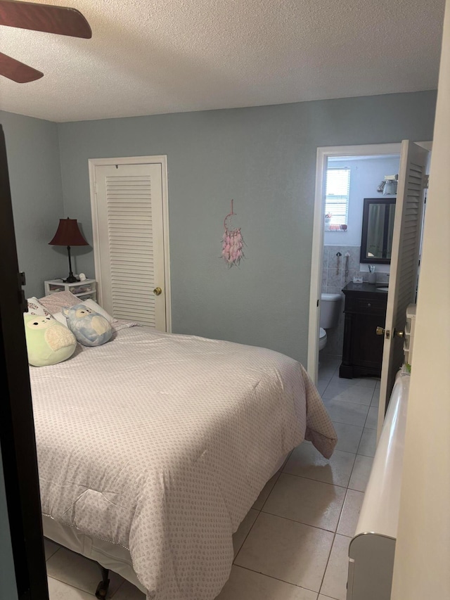 bedroom with a textured ceiling, ensuite bathroom, ceiling fan, light tile patterned flooring, and a closet