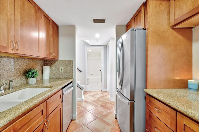 kitchen with backsplash, light stone countertops, stainless steel appliances, and light tile patterned floors