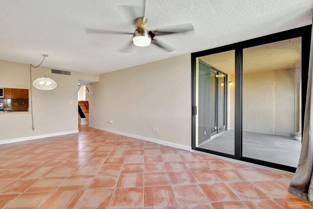 tiled empty room featuring ceiling fan, a textured ceiling, and a wall of windows