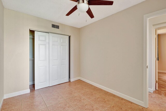 unfurnished bedroom with ceiling fan, a closet, light tile patterned floors, and a textured ceiling