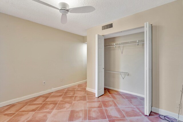 unfurnished bedroom with tile patterned floors, ceiling fan, a closet, and a textured ceiling