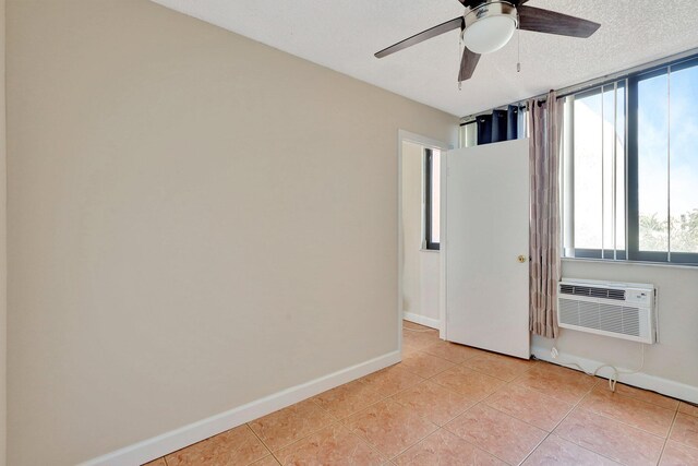 empty room with a wall mounted air conditioner, light tile patterned floors, a textured ceiling, and ceiling fan