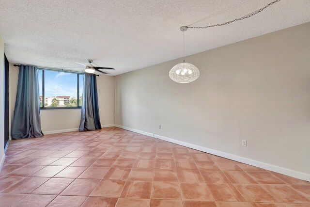 tiled empty room featuring ceiling fan with notable chandelier and a textured ceiling