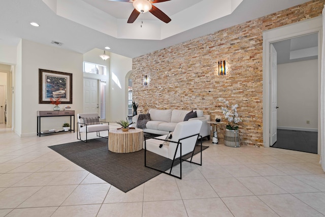 tiled living room with a high ceiling, a raised ceiling, and ceiling fan