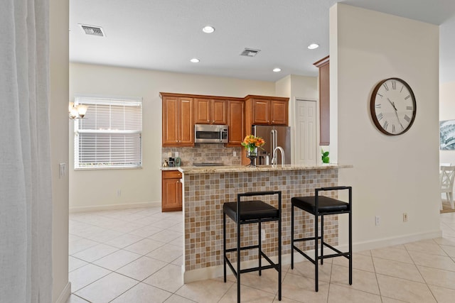 kitchen featuring a kitchen breakfast bar, light tile patterned floors, stainless steel appliances, and a notable chandelier