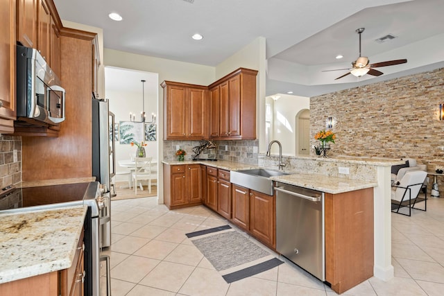 kitchen with sink, light tile patterned floors, appliances with stainless steel finishes, light stone counters, and kitchen peninsula