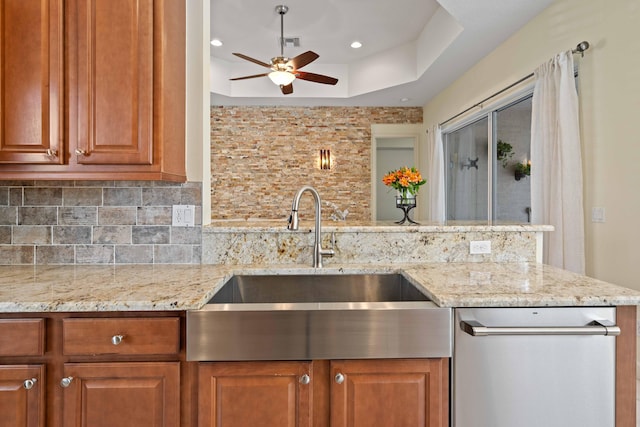 kitchen with backsplash, sink, ceiling fan, light stone countertops, and a tray ceiling