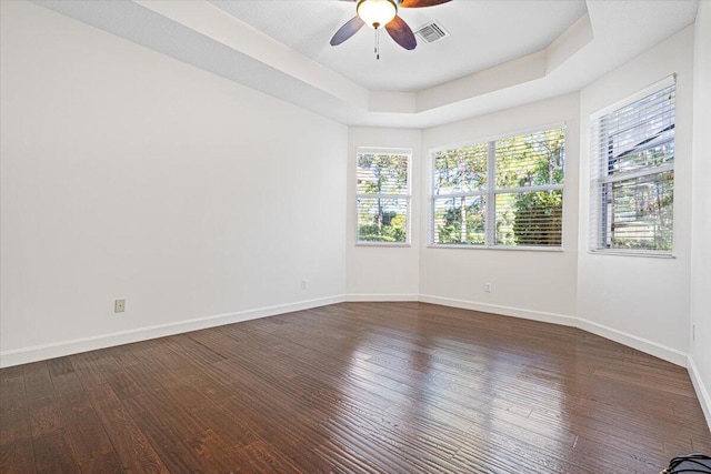 empty room with a raised ceiling, ceiling fan, and dark hardwood / wood-style flooring