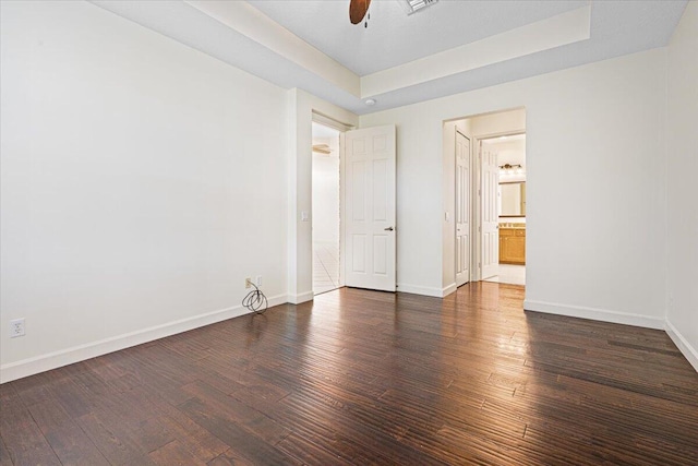 empty room with a tray ceiling, ceiling fan, and dark hardwood / wood-style floors