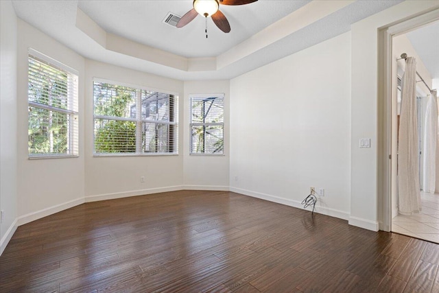 spare room with a raised ceiling, ceiling fan, and dark hardwood / wood-style flooring