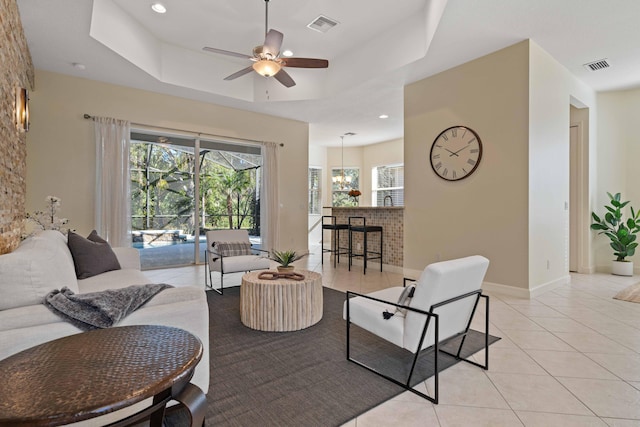 tiled living room featuring a raised ceiling, plenty of natural light, and ceiling fan with notable chandelier