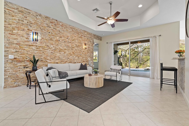 living room featuring a tray ceiling, ceiling fan, and light tile patterned flooring